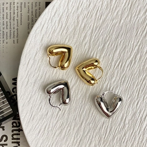 Pendientes de aro con forma de corazón hueco en oro y plata sobre bandeja de cerámica