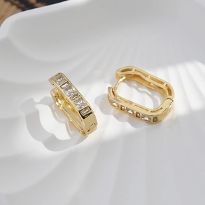 Detail of luxury gold brass hoop earrings with white zircon on a white shell plate