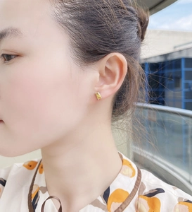 Detail view of a rectangular yellow zircon stud earring on a model in outdoor lighting