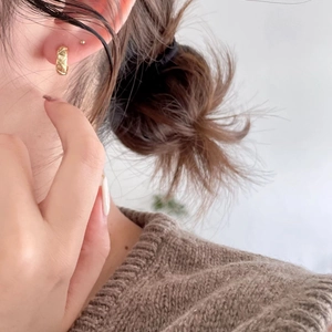 Detail of gold quilted pattern hoop earring worn on ear showing high-shine metal finish
