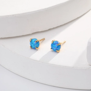 Macro shot of blue opal stud earrings in golden 4-prong setting on geometric stand