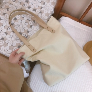 Detail of cream canvas tote bag featuring brown leather handles and metal rivet reinforcement