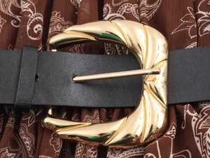 Dettaglio macro di cintura in pelle nera con fibbia dorata testurizzata sul vestito