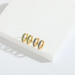Detail view of gold huggie earrings with emerald and sapphire stones on white stone
