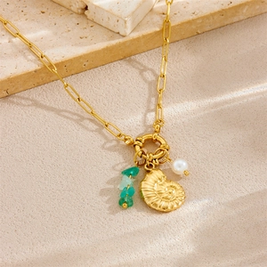 Gold chain necklace with shell pendant, green stone beads and pearl on textured surface