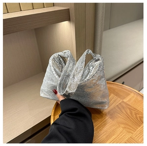 Gros plan d'un sac baguette à paillettes argentées tenu par un mannequin sur une table