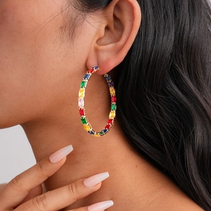 Close-up of model wearing large gold hoop earrings with multi-colored rectangular zircon stones