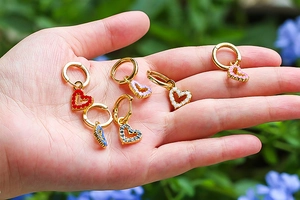 Detailed view of colorful enamel heart earrings in gold finish held in palm