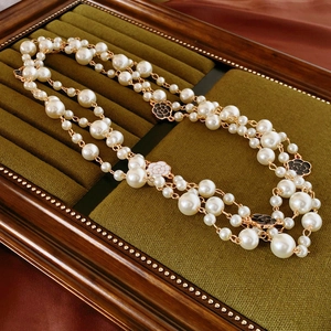 Macro detail of camellia flower pendants and white baroque pearls on a gold chain necklace