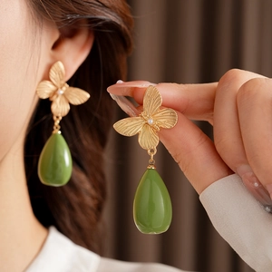 Détail de boucles d'oreilles papillon dorées vintage avec perle et goutte de résine verte