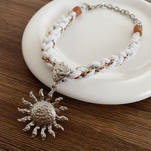 Detail of silver sun pendant on white woven cord necklace with metallic clasp