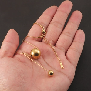 Detail of gold stainless steel necklace featuring double sphere pendants and tassel