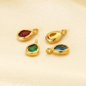 Macro shot of stainless steel teardrop pendants with colorful stones on silk fabric