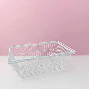 Close-up of a white iron wire storage basket with dual handles on a pink background
