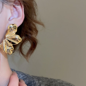 Detailed view of irregular wavy gold earrings with a molten lava texture on a model's ear