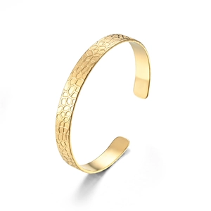 Detail of gold-colored cuff bracelet showing intricate geometric honeycomb engraved texture