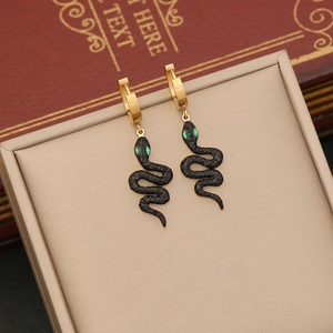 Golden hoop earrings with black snake pendants on a beige jewelry box with vintage book