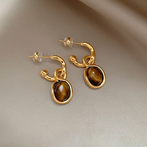 Detailed close-up of gold-plated oval tiger eye earrings on soft champagne silk fabric