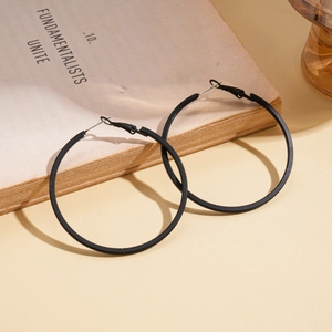 Macro view of matte black leather-wrapped geometric hoop earrings on a vintage book edge