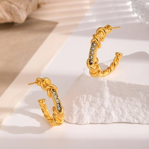 Elegant gold twisted C-shape earrings with inlaid zircon on white stone background