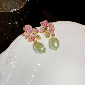 Macro detail of gold-plated floral earrings with pink petals and green pearl pendant