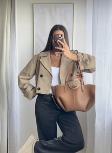 Detail of a chic beige short double-breasted trench coat paired with a brown tote bag