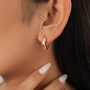 Detail of golden textured hoop earring with crumpled metal design on model's ear