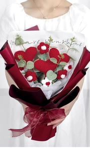 Close-up of hand-knitted heart and flower bouquet in red paper wrap with ribbon
