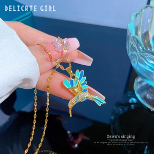 Detail of a gold hummingbird pendant necklace with blue enamel wings and shiny white rhinestones