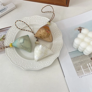 Close-up of three triangle-shaped brocade Zongzi charms with colorful woven cords in a white bowl