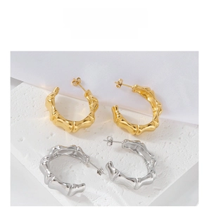 Close-up of gold and silver bamboo-style C-shaped stud earrings on a stone display