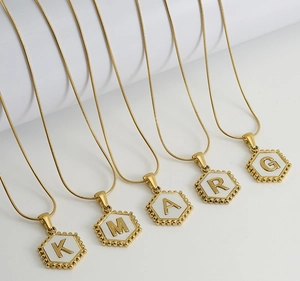 Detail of five gold hexagon initial necklaces with shell white inlay and bead edging