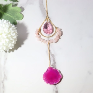 Macro shot of natural agate slice and pink teardrop crystal on a golden chain