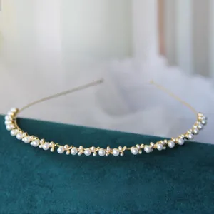 Dettaglio di un cerchietto dorato con perle bianche su un supporto in velluto verde scuro