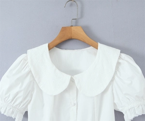 Dettaglio camicia bianca con maniche a sbuffo, ricami in pizzo e colletto Peter Pan