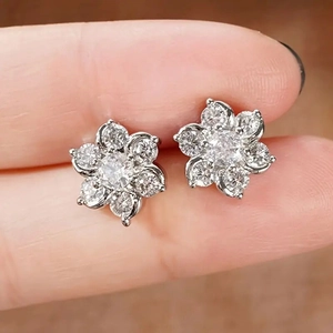 Elegant floral zircon stud earrings in sparkling silver finish held in hand for scale