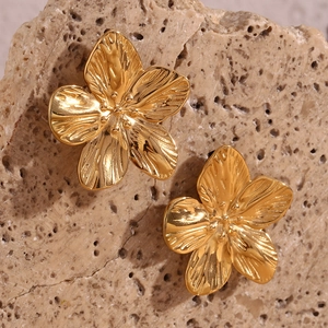 Macro detail of 18K gold plated petal earrings on natural stone surface background