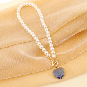 Close-up of white pearl necklace with blue heart-shaped faceted gemstone and T-bar toggle