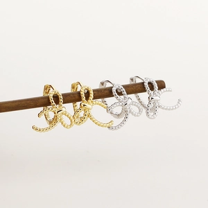 Detailed view of silver and gold twisted rope bow earrings on a wooden display