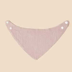 Pink cotton muslin baby bandana bib with adjustable snaps on a warm neutral background
