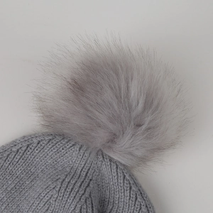 Close-up of grey knitted beanie with dense texture and plush faux fur pompom detail