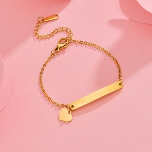 Detail of gold-plated stainless steel bar bracelet with heart charm on pink background