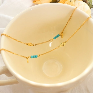 Gold titanium anklet with turquoise beads and wing charms in a ceramic cup