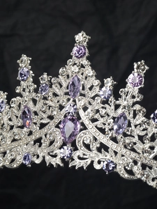 Close-up of silver princess crown with purple gems and rhinestones on black fabric