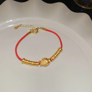 Détail d'un bracelet tressé rouge avec breloque poisson dorée et perles en métal