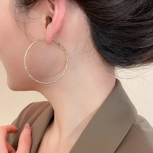 Detailed close-up of large golden hoop earrings with elegant twisted spiral texture