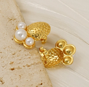 Detail of gold textured earrings with three white pearls on raw stone and silk background