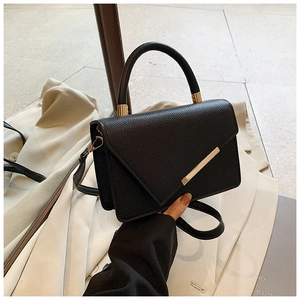 Detail of black lychee grain leather crossbody bag with elegant gold metal ring accents