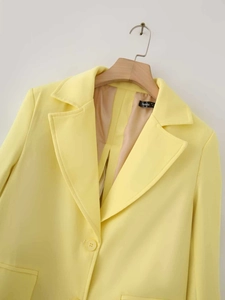 Detail of light yellow satin blazer featuring classic single-breasted cut on a wooden hanger