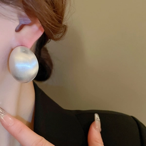 Close-up of minimalist brushed metal oval earrings worn by a model in a studio setting